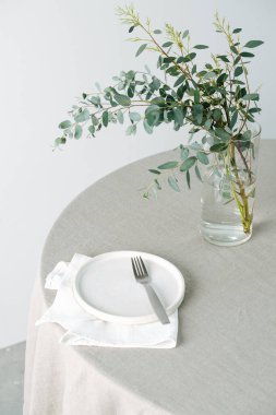 Boş tabak ve yuvarlak masa, kaba bir masa örtüsü ve kavanozda bir dal.
