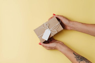 Kadın eli, sarı bir yüzeye etiketli karton kutu yerleştiriyor.