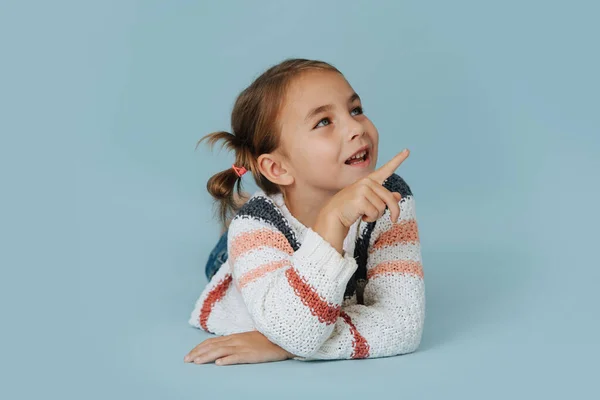 穿着条纹毛衣的社交小女孩躺在地板上 背景是蓝色的 一边用食指说话一边跟别人说话 — 图库照片