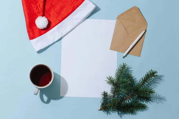 Colocação plana de uma folha de papel em branco, chapéu de Natal, caneca, caneta e envelope. — Fotografia de Stock