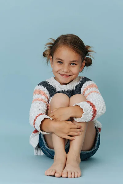 Щаслива маленька дівчинка в смугастому светрі сидить на підлозі над синім Ліцензійні Стокові Фото