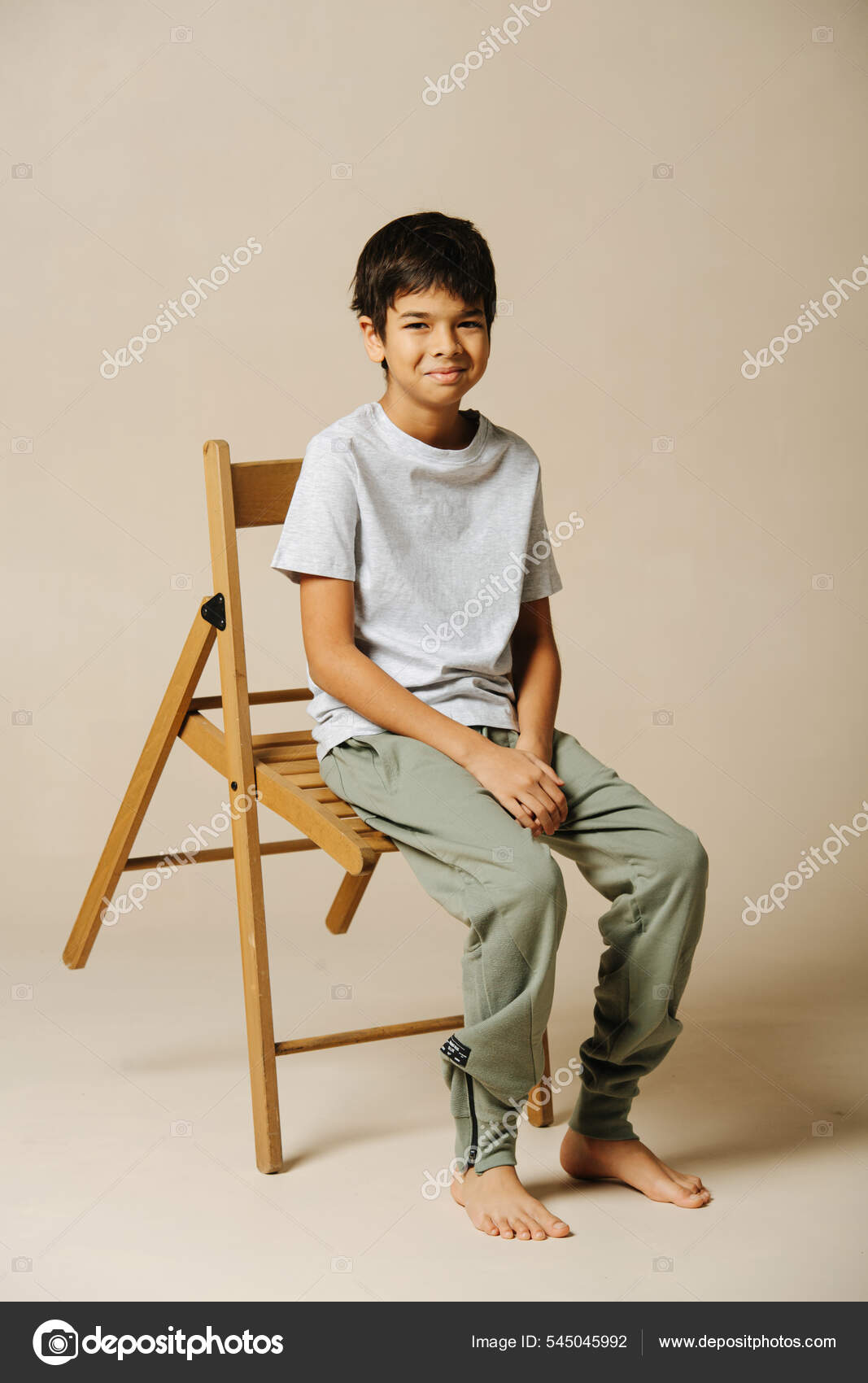 Amused Indian Boy Sitting Wooden Folding Chair Beige Room Leaning