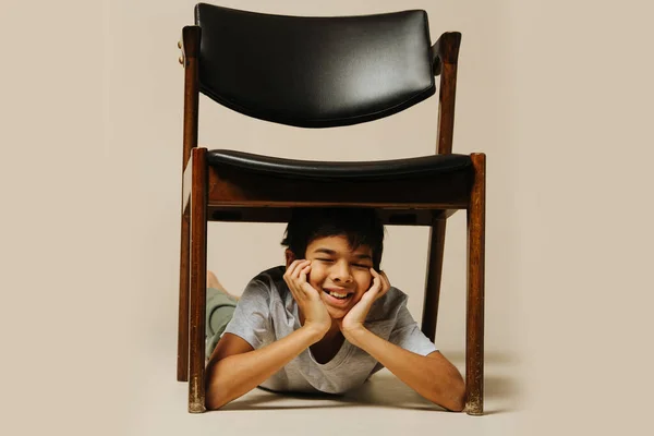 无忧无虑的印第安男孩坐在扶手椅下玩耍 眼睛闭着 双手靠着 米色背景 — 图库照片