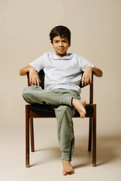 Крутий Впевнений Індійський Хлопчик Сидить Кріслі Кімнаті Над Бежевим Тлом — стокове фото