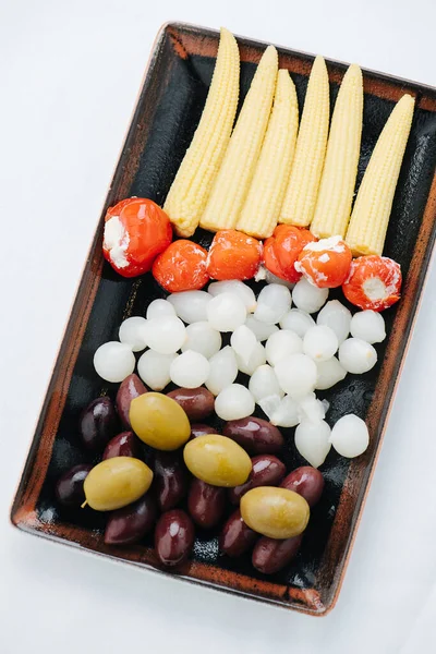 Vegetables on a wooden tray. Corn, suffed tomatoes, onions and olives. — Stock Photo, Image