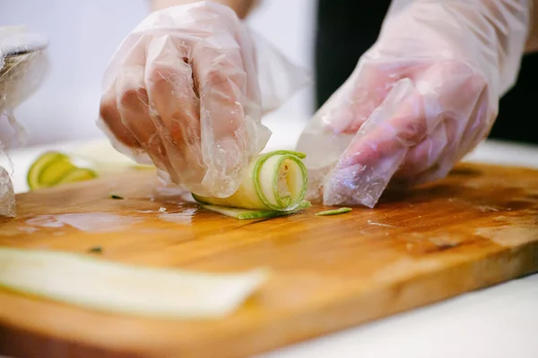 Hands in single use plastic gloves making a roll out of thin cucumber slice — Stock Photo, Image