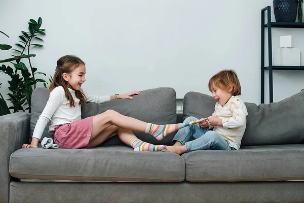 男孩脱下女孩的袜子 他们正在准备参加一个挠痒痒的比赛 坐在客厅的沙发上 侧视图 免版税图库图片