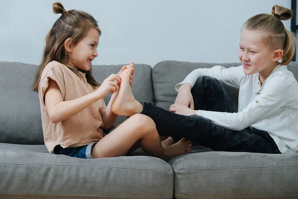 Mischievous girl trying to tickle boy\'s foot, they both laugh. On the couch side view.