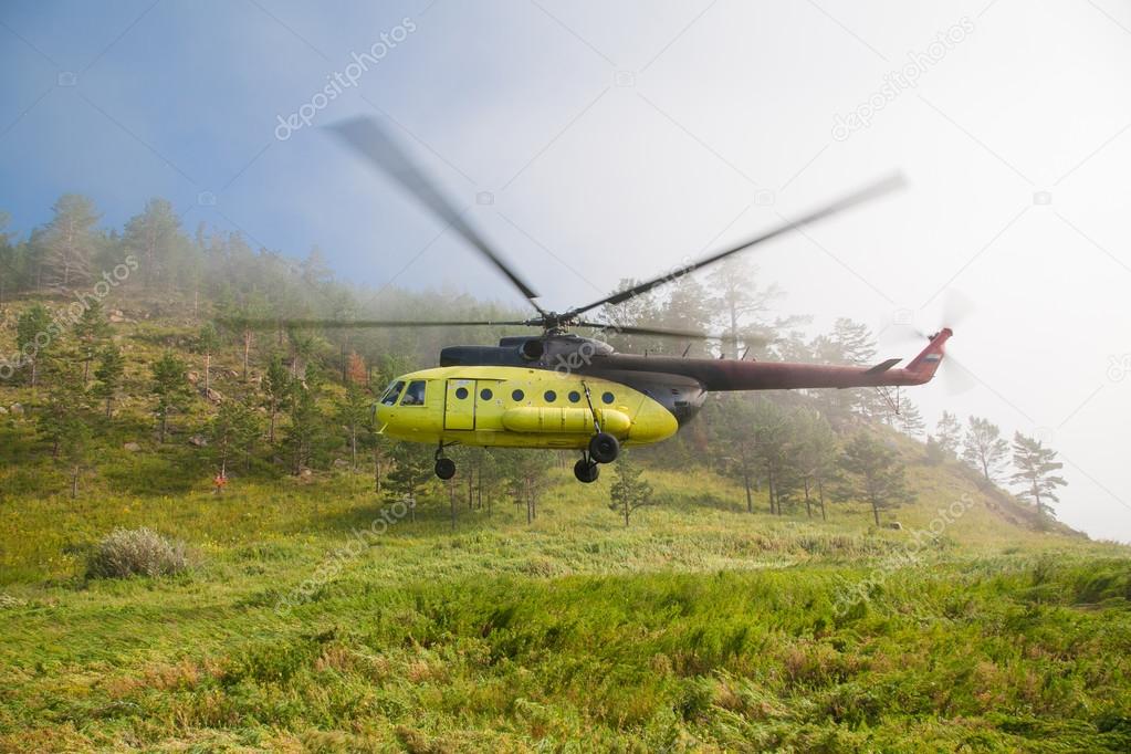 Large helicopter lands in the forest in the fog.