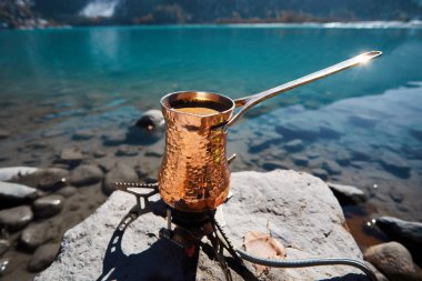 Copper Cezve sonbahar gölünde kahve için dağlarda kamp yapıyor. Gaz ocağında kahve hazırlamak kamp konsepti. 