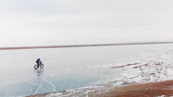 Flygfoto av man ridning cykel vid frusen sjö. — Stockvideo