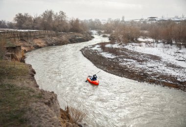 Adam kışın nehirde turuncu botta kürek çekiyor..