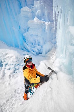 Almaty, Kazakistan 'daki dağlarda donmuş şelalenin yanında buzdan baltayla turuncu ceketli bir kadın tırmanıyor.