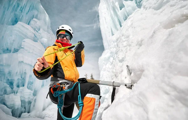 Buz şelalesinin yanındaki buz baltası ve turuncu ceketli iple dağcı portresi.