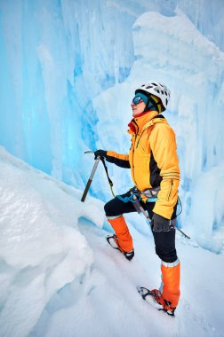 Donmuş şelalenin yanında turuncu ceketli buz baltasıyla dağlara tırmanan bir kadın. Spor dağcılığı ve dağcılık konsepti.