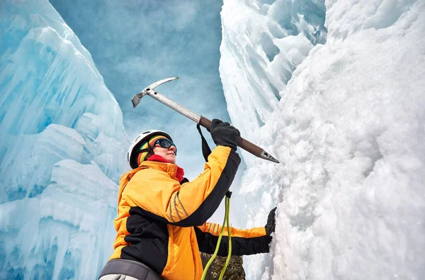 Woman is climbing frozen waterfall with ice axe in orange jacket in the mountains. Sport mountaineering and alpinism concept.