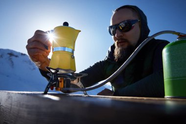 Sakallı adam yürüyüşçüsü. Sarı Moka kahve demliğinden kahve yapıyor. Karlı kış dağlarında gaz ocağında. Kamp yapmak için eski tarz kahve.