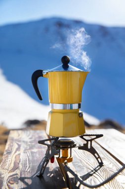 Karlı dağ kampında buharlı sarı moka otu kahvesi. Sabah pikniği, doğada kahvaltıda sıcak içecek pişiren kişi.