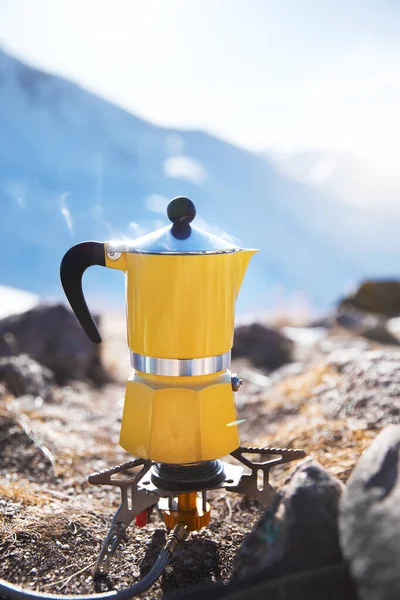 Karlı dağ kampında buharlı sarı moka otu kahvesi. Sabah pikniği, doğada kahvaltıda sıcak içecek pişiren kişi. Dikey çekim