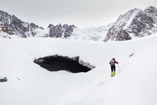 在哈萨克斯坦阿拉木图美丽的高山山谷被雪覆盖的风景中 背着背包在冰洞拱顶附近的游客们正在冰河边游览 — 图库照片
