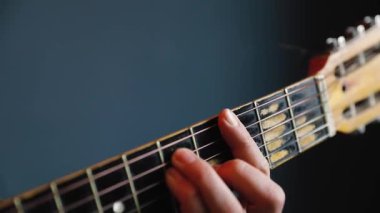 Adam mavi duvarda akustik gitar çalıyor.