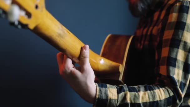 Człowiek gra na gitarze akustycznej na niebieskiej ścianie — Wideo stockowe