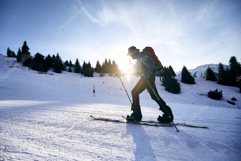 Skier man ski touring uphill with beard and backpack at high snowy mountain ski resort Shymbulak. Sport outdoor backcountry winter season.