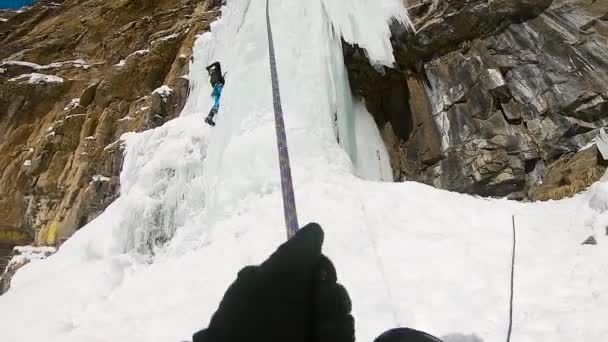 Человек взбирается на ледяной водопад с помощью веревки и ледоруба — стоковое видео