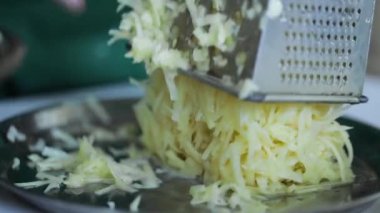 Aşçı mutfakta patatesi rendeleyiciye sürter.