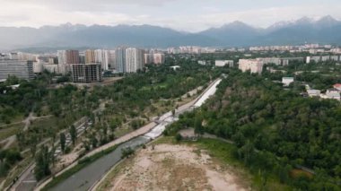Almaty, Kazakistan 'da güneş doğarken Sairan Gölü yakınlarında gökdelenler ve dağ manzaralı nehrin görüntüsünü çektik.