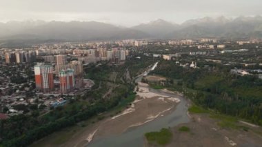 Almaty, Kazakistan 'da güneş doğarken Sairan Gölü yakınlarında gökdelenler ve dağ manzaralı nehrin görüntüsünü çektik.