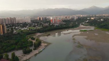Almaty, Kazakistan 'da güneş doğarken Sairan Gölü yakınlarında gökdelenler ve dağ manzaralı nehrin görüntüsünü çektik.