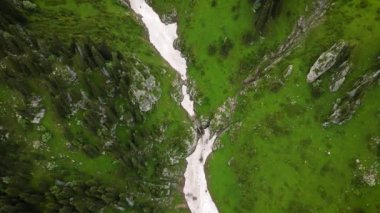 Yeşil orman dağ vadisinde şelaleli beyaz kar buzulu. Yukarıdan aşağıya hava aracı tarafından çekilen hava görüntüsü.