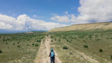 Dağ bisikletleriyle dağ vadisine giden yolda mavi bulutlu gökyüzüne karşı bisiklet süren insanlar. Eğlence ve sağlıklı yaşam tarzı konsepti hava aracı çekimi.