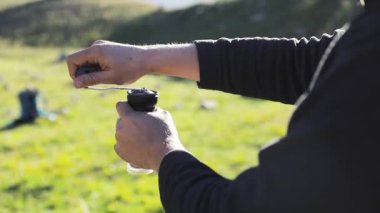 Göldeki kayalıklarda siyah öğütücüde taze kahve çekirdeklerini öğüten, kampta alternatif kahve demleyen adam. Açık havada piknikte sıcak içecek yapmak. Dağlarda trekking ve yürüyüş