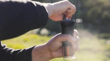 Göldeki kayalıklarda siyah öğütücüde taze kahve çekirdeklerini öğüten, kampta alternatif kahve demleyen adam. Açık havada piknikte sıcak içecek yapmak. Dağlarda trekking ve yürüyüş