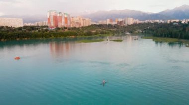 Man at stand up paddle boards SUP in the mountain lake Sairan in city Almaty in Kazakhstan. Drone shot aerial outdoor activity