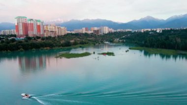 Boat and catamaran in the mountain lake Sairan in city Almaty with skyscrapper building in Kazakhstan. Drone shot aerial outdoor activity