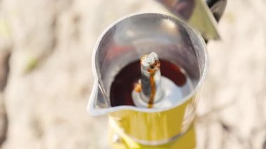 Man making boil coffee in yellow moka pot from grinded fresh coffee at nature, brewing espresso alternative coffee at camping. Making hot drink at picnic outdoors. Trekking and hiking in mountains