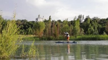 Man at stand up paddle boards SUP in the mountain lake Sairan in city Almaty near Orthodox Church in Kazakhstan.