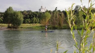 Man at stand up paddle boards SUP in the mountain lake Sairan in city Almaty near Orthodox Church in Kazakhstan.