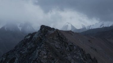 Hava aracı, Kazakistan 'da bulutlu bulutlu bir gökyüzü olan dağ vadisinde buzullu ve kayalık duvarlı kar zirvesi görüntülerini ortaya çıkardı.