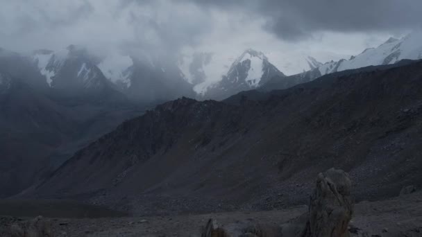 空中ドローンの風景は カザフスタンの曇った暗い空を持つ山の谷の氷河と岩壁で雪の頂上のショットを明らかにする — ストック動画