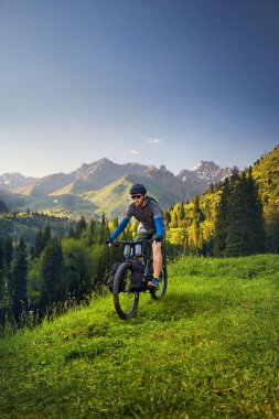 Sarışın ve sakallı bir adam, Kazakistan, Almaty 'de gün batımında güzel dağ vadisindeki yeşil tepe ormanlarında turist çantalarıyla dağ bisikletine biniyor. Extreme Sport bisiklet paketleme ve açık hava eğlence konsepti.