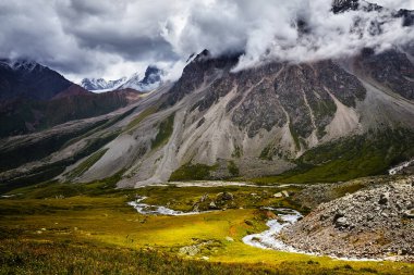Sırt çantalı iki Yürüyüşçü, dağ vadisinde sise ve karanlık bulutlu gökyüzüne karşı nehrin yanındaki tepede yürüyor. Açık hava ve yürüyüş konsepti.