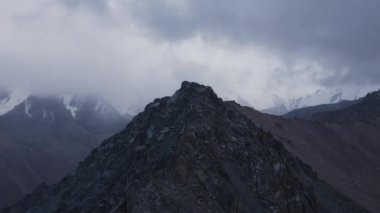 Hava aracı, Kazakistan 'da bulutlu bulutlu bir gökyüzü olan dağ vadisinde buzullu ve kayalık duvarlı kar zirvesi görüntülerini ortaya çıkardı.