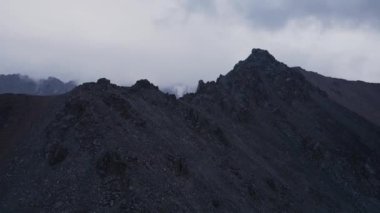 Hava aracı, Kazakistan 'da bulutlu bulutlu bir gökyüzü olan dağ vadisinde buzullu ve kayalık duvarlı kar zirvesi görüntülerini ortaya çıkardı.