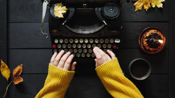 一个穿着黄色毛衣 用黑色老式打字机书写的年轻女子的手从桌上弹出 秋天的叶子 咖啡和蛋糕加蜡烛 — 图库视频影像