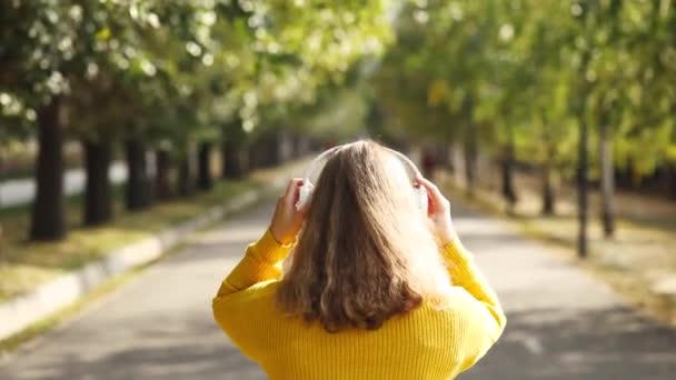 Kobieta Zakłada Białe Słuchawki Głowę Słucha Muzyki Jesiennym Parku Żółtym — Wideo stockowe