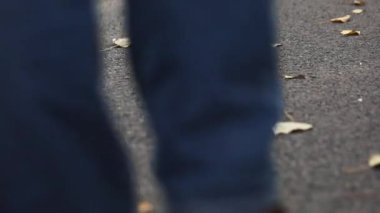Kahverengi deri ayakkabılı bir kızın bacakları sonbahar yaprakları arasında yolda yürüyor.